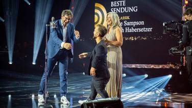 Beate Sampson und Ulrich Habersetzer gewinnen den Radiopreis in der Kategorie "Beste Sendung". Mathias Mester übergibt den Preis. © Deutscher Radiopreis / Benjamin Hüllenkremer Foto: Benjamin Hüllenkremer