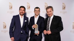 Adrian Feuerbacher und Benedikt Strunz freuen sich mit Laudator Günther Oettinger den Radiopreis für das "Beste Nachrichten- und Informationsformat".  Foto: Morris Mac Matzen