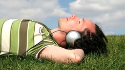 Ein junger Mann mit Kopfhörern liegt im Gras und hört Musik. © Edyta Pawlowska - Fotolia Foto: Edyta Pawlowska
