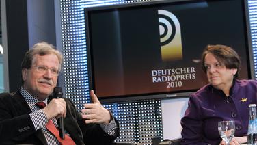 Uwe Kammann und Prof. Dr. Karin von Welck in zwei Sesseln um einen kleinen Tisch mit Getränken sitzend. Uwe Kammann redet. Im Hintergrund ein Bildschirm mit dem Logo des Deutschen Radiopreis 2010. © NDR Foto: Marcus Krüger