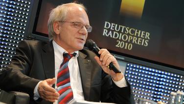 Pressekonferenz zur Vorstellung des Deutschen Radiopreises am 4.2.2010: Lutz Kuckuck sitzt redend in einem Sessel. Im Hintergrund ein Bildschirm mit dem Logo des Deutschen Radiopreis 2010. © NDR Foto: Marcus Krüger