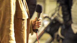 Eine Person mit Mantel hält ein Mikrofon in der Hand. © fotolia Foto: wellphoto