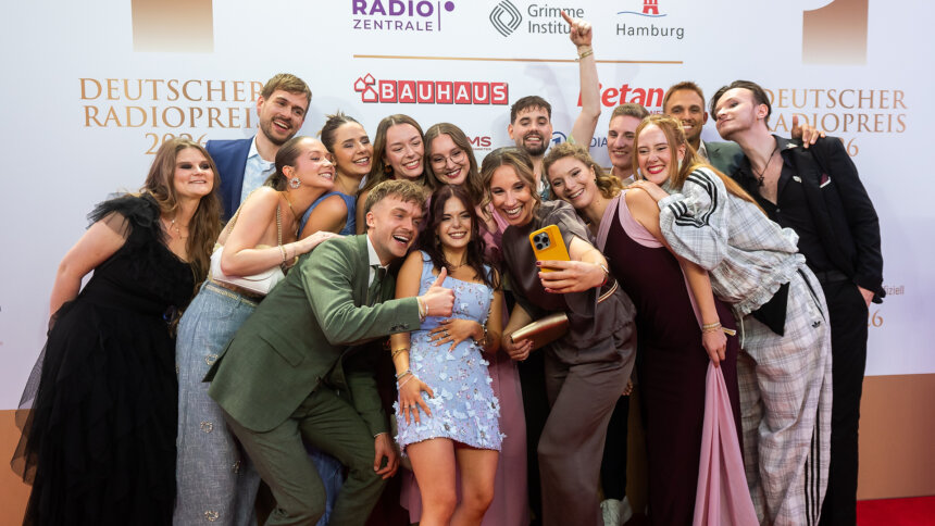 Die nominierten Newcomer:innen posen für ein Selfie vor der Logowand.
